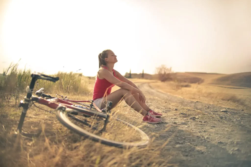 Sporty woman with bicycle resting on countryside road in sunlight