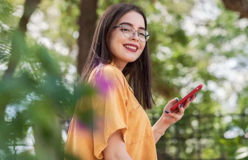 A smiling girl wearing glasses checking out counseling online on her smart phone.